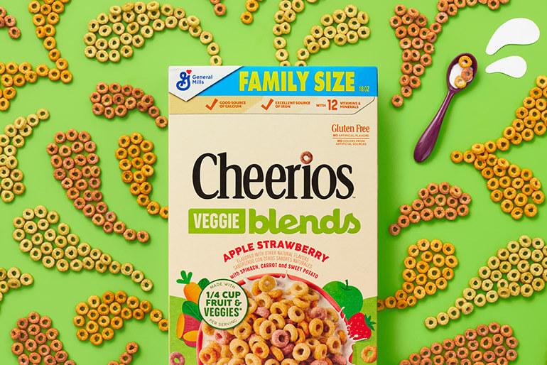 A box of Cheerios apple strawberry veggie blends cereal on a green cereal pattrened background.