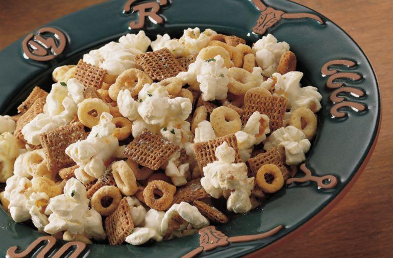 Cheerios, Multi-Bran Chex, and popcorn tossed with ranch dressing in a bowl.