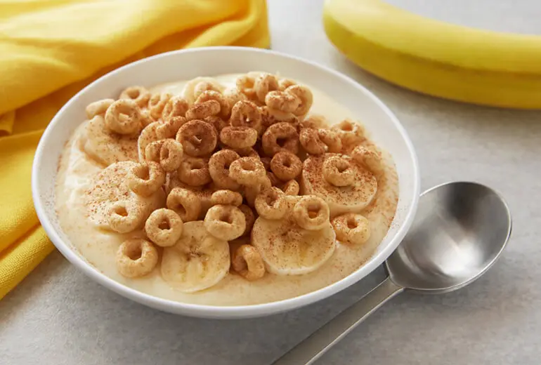 Fat-free yogurt and sliced banana topped with Honey Nut Cheerios and baking cocoa in a bowl.