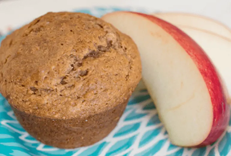 A Cheerios Applesauce Muffin with slices of apple next to it on a plate.