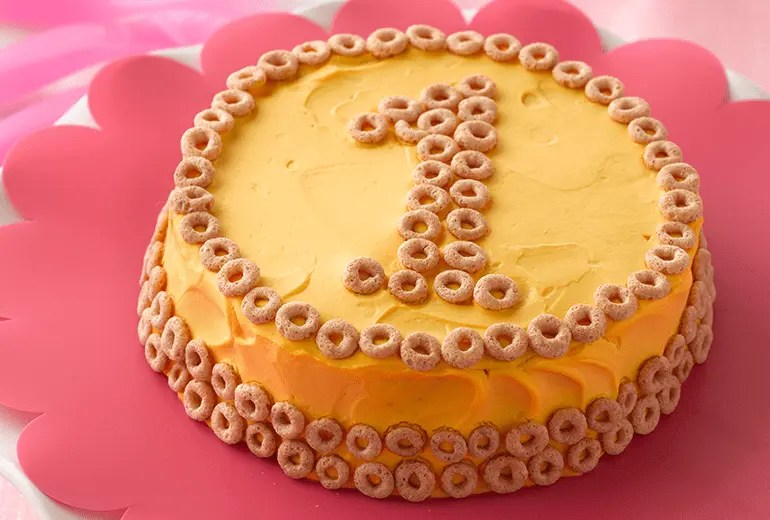 Orange birthday cake made with Betty Crocker yellow cake mix, frosted with cream cheese and Cheerios cereal pieces.