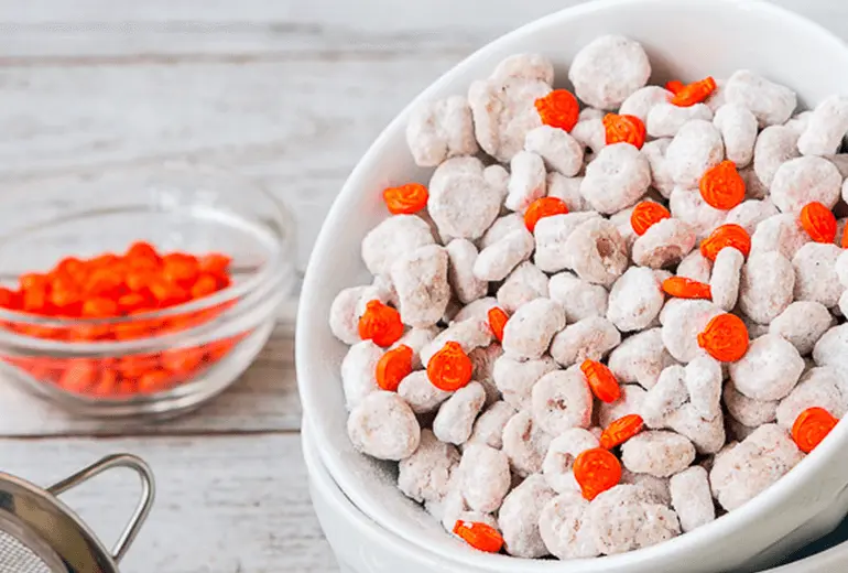 Cheerios and Pumpkin Spice Puppy Chow coated in powdered sugar in a white bowl.