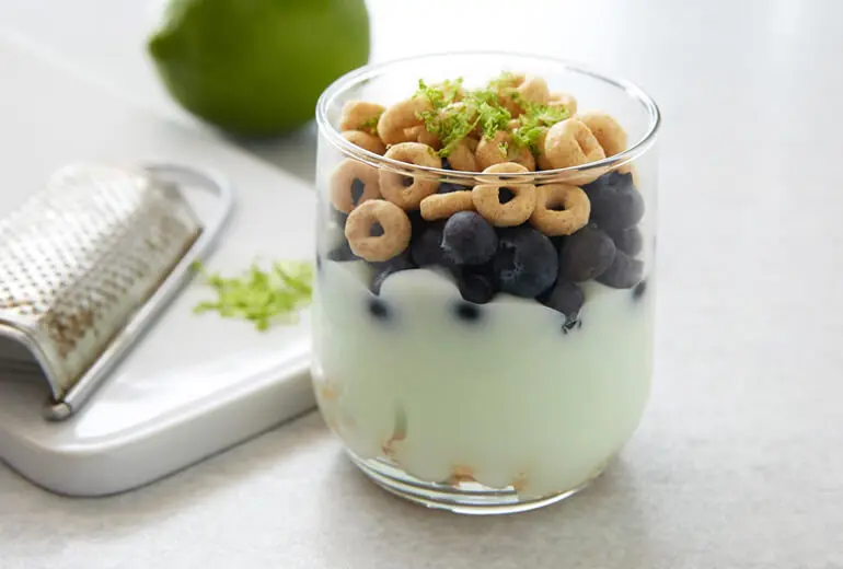 Honey Nut Cheerios, key lime pie yogurt, and fresh blueberries in a glass with a lime and grater in the background.