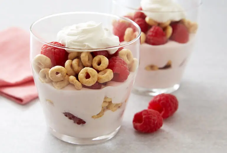 Two parfaits with raspberry yogurt, layered with fresh raspberries and Honey Nut Cheerios in glasses.