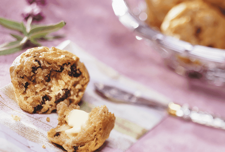 A banana muffin with cereal baked in split open to expose the middle topped with melting butter.