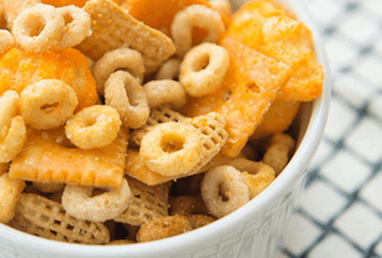 Multi grain Cheerios cereal, cheese crackers and puffcorn topped with Parmesan cheese in a white bowl.