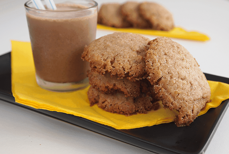 4 Non-Dairy Crumbly Cheerios Cookies on a plate with a cup of chocolate milk next to them.