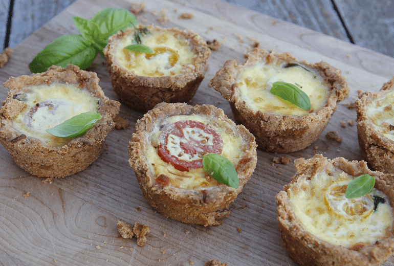 Six cheese, tomato and basil quiches with a Cheerios crust on a wooden serving board.