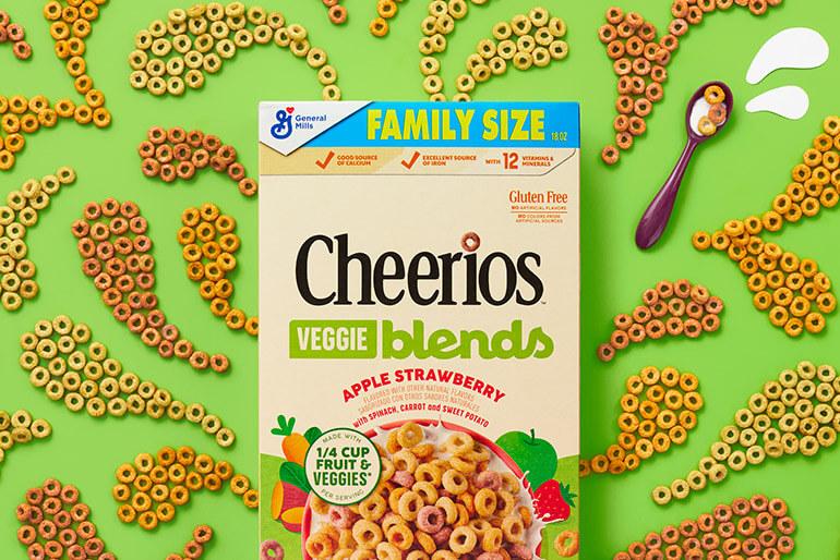 Una caja de vegetales Cheerios, manzana, fresa, mezcla cereales sobre un fondo verde con patrón de cereales.