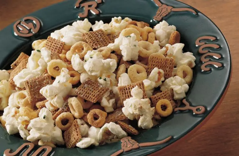 Cheerios, Multi-Bran Chex, and popcorn tossed with ranch dressing in a bowl.