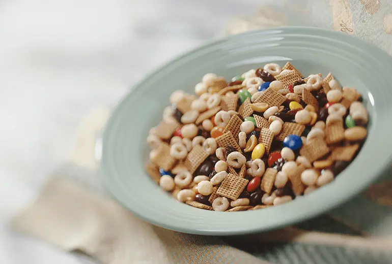 Trail mix made with Cheerios, Chex, Kix, raisins and chocolate candies in a bowl.