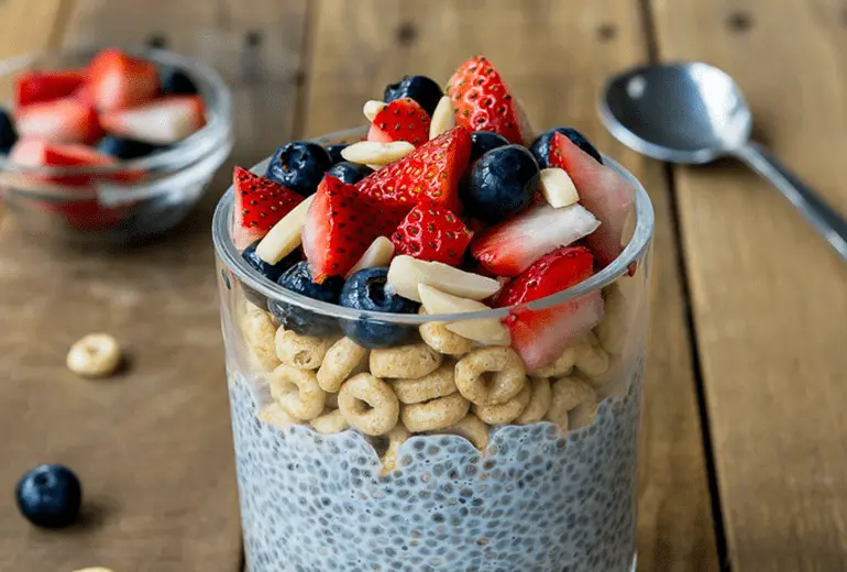 Chia Pudding layered with Cheerios, fresh berries, and almonds in a glass with a spoon.