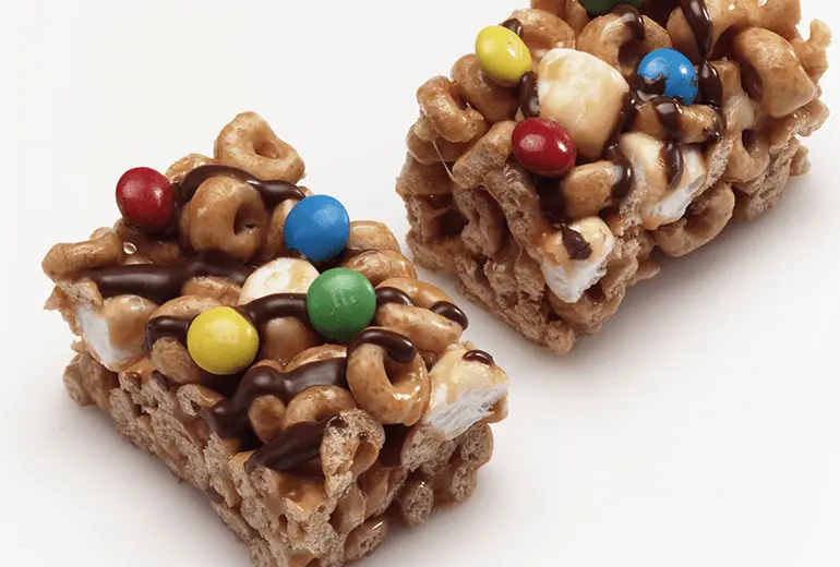 Two Gluten-Free Cheerios Caramel Crisp Cereal Bars topped with candy-coated chocolate candies.