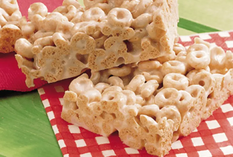Two squares of Cheerios cereal bars made with melted buttered and marshmallows.
