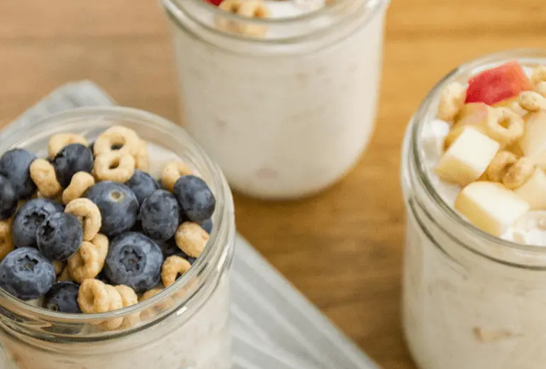 Three jars of cereal, fruit and oatmeal topped with fruit and Cheerios.
