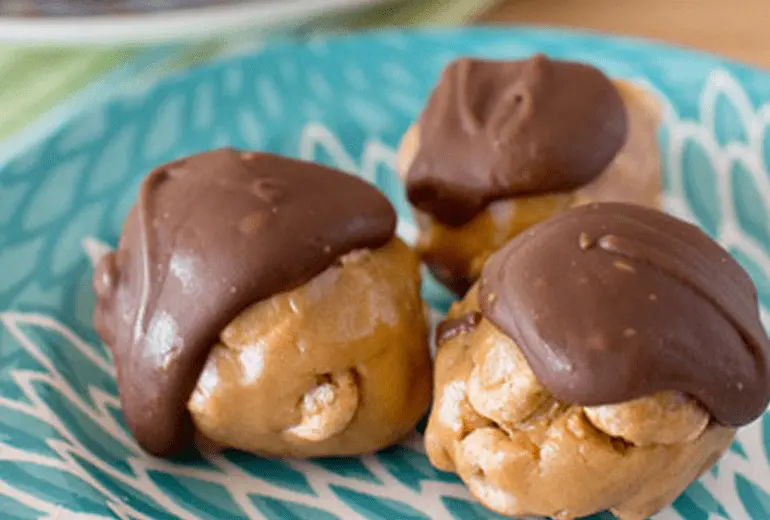 Three gluten-free peanut butter and Cheerios chocolate-covered balls on a decorative plate.