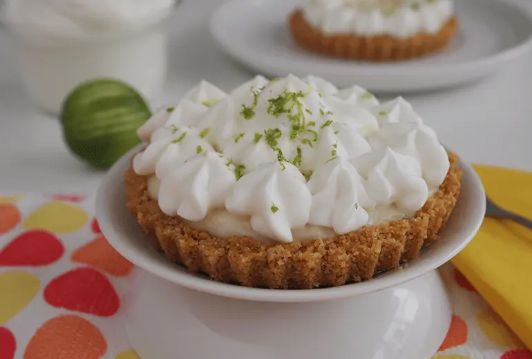A Lime Juice Tartlet with ground Cheerios crust topped with heavy cream on a serving plate.