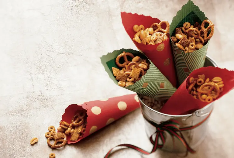 Snack mix in 5 paper cones made with Cheerios, pretzels, peanuts, and Worcestershire sauce.