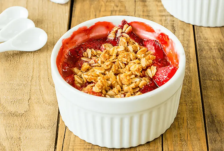 Baked strawberry crisp with Cheerios topped with oats in a white ramekin.