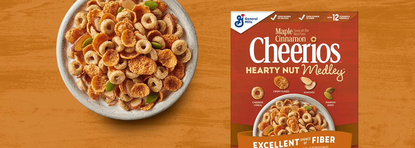 A bowl of Cheerios Maple Cinnamon Hearty Nut Medley Cereal next to the Cheerios Maple Cinnamon Hearty Nut Medley Cereal box.