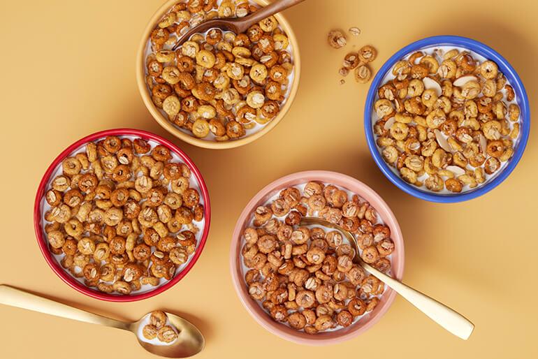Four bowls of Cheerios Oat Crunch cereal with milk and spoons.