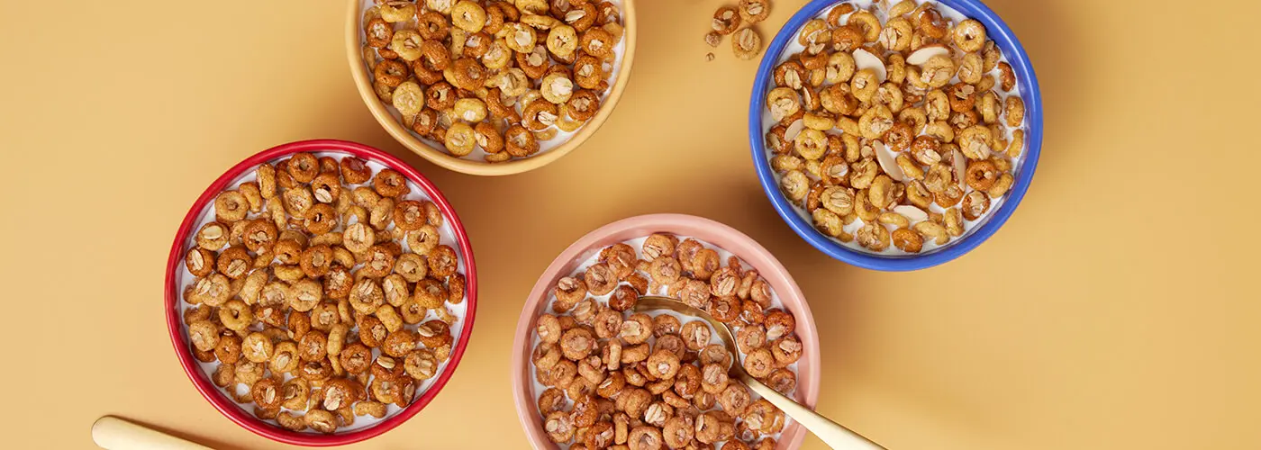 Four bowls of Cheerios Oat Crunch cereal with milk and spoons.