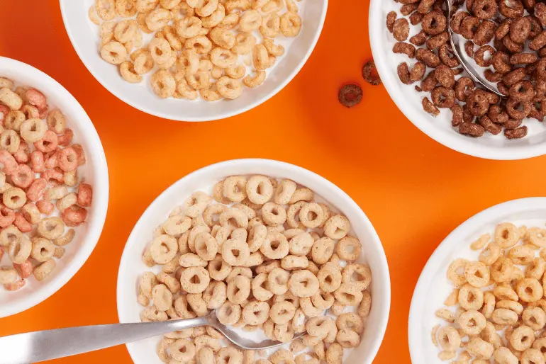 Bowls of various types of cheerios breakfast cereals on an orange background.